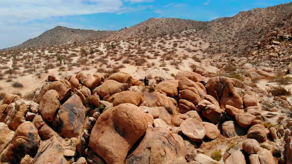 A Man stands on a Mountain made of Rocks looking out over a barren desert in Joshua Tree on his own,