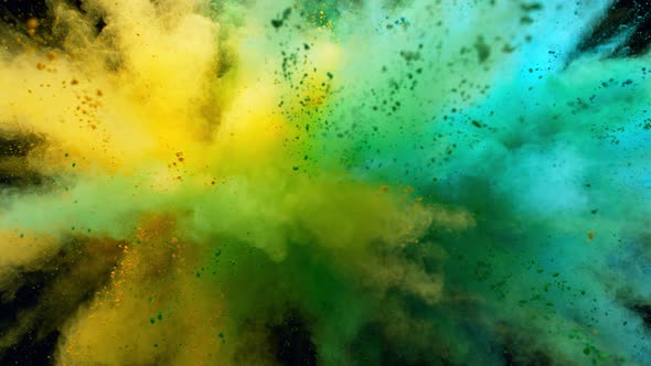 Colorful powder/particles fly after being exploded against black background. Slow Motion.