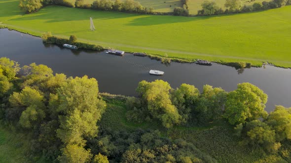 Boat sailing on river Thame and shores with green grassland, Mapledurham in UK. Aerial top-down orbi
