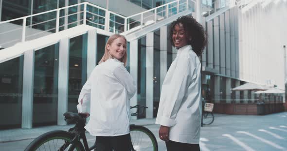 Two young women in business attire, with a bike in a business area