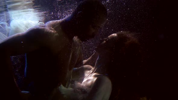 Man and Woman Are Embracing Underwater in Darkness, Subaquatic Magical Shot