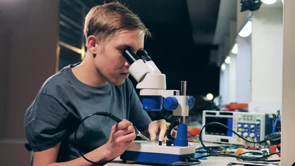 Repair Specialist Looking Through Microscope System Board Soldering