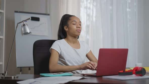 Charming Slim Young Woman Stretching in the Morning Sitting at Table with Laptop in Home Office