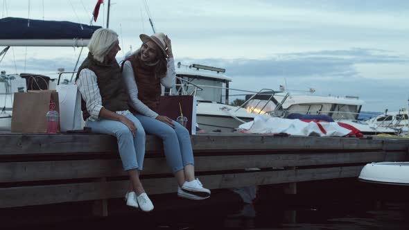 Two Cheerful Women Sitting on Pier after Shopping