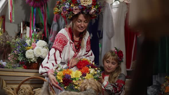 Happy Ukrainian Mother and Daughter with Flowers Smiling Standing Indoors with Little Dog