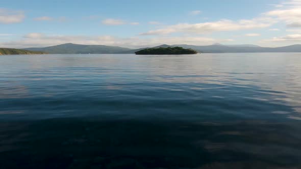 View from a boat on the driving towards a lone island in the center. Marlborough Sounds. Near Picton