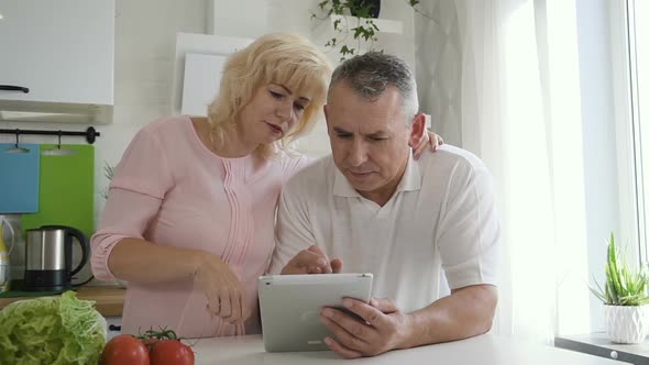 Mature Woman Explaining Senior Husband How To Use Tablet Computer