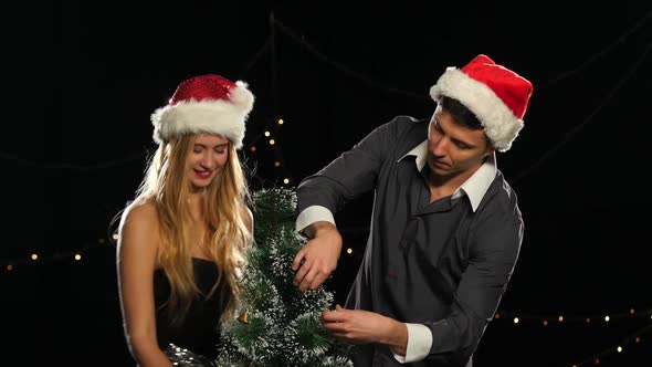 Beautiful Couple in Christmas Hats Decorating a Christmas Tree on Black