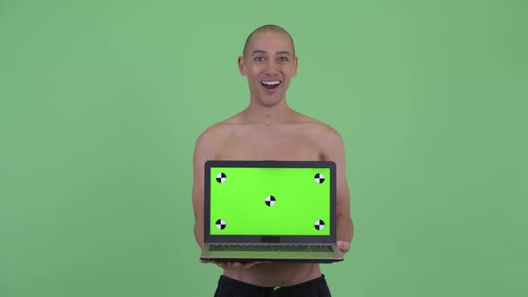 Happy Bald Multi Ethnic Shirtless Man Showing Laptop and Looking Surprised