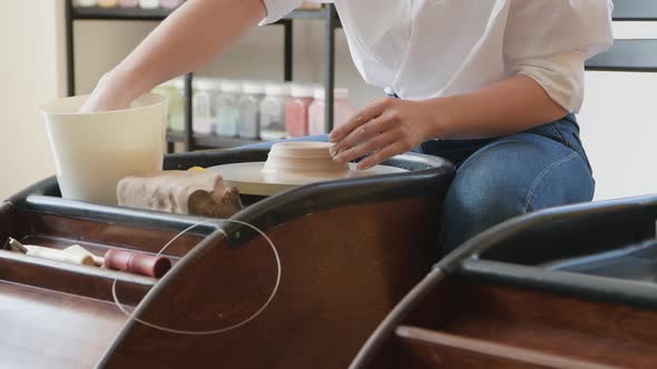 Closeup of Young Female Potter with Sponge Keeping It Close To Rotating Clay Pot While Shaping Form