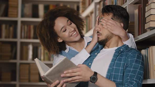 Young Hispanic Male Student Stands in Library Reading Book African American Girl Unexpectedly