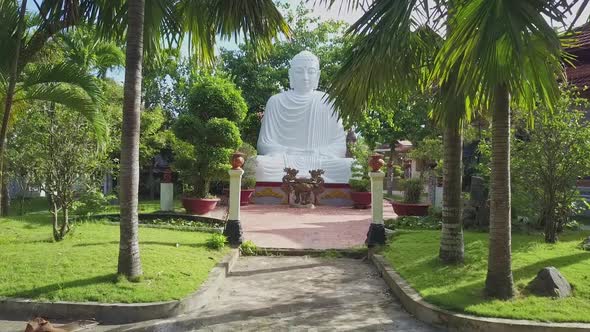 Drone Approaches To White Buddha Statue Among Tropical Plants