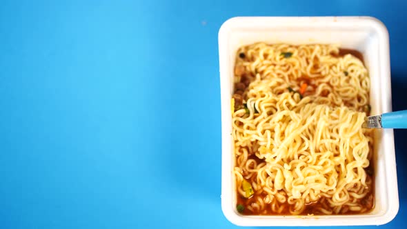 Close Up of Instant Noodles with Spices on Blue Background. Woman's Hand Screwing Macaroni on Fork.