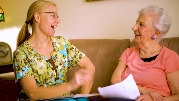 Closeup of elderly woman and home healthcare nurse laughing and going over paperwork.