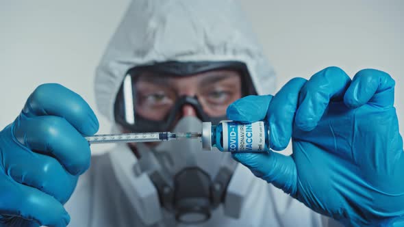 Portrait of Doctor in Protective Suit Fills Syringe with Coronavirus Vaccine Preparing for Injection