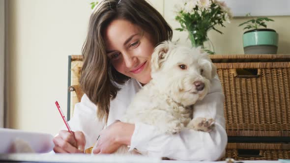 Caucasian woman drawing working from home and cuddling her pet dog