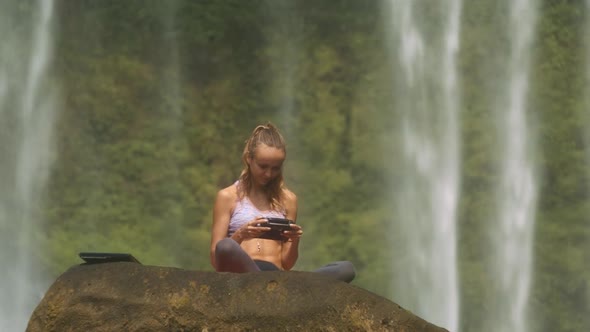 Woman Watches Video on Tablet Against Waterfall