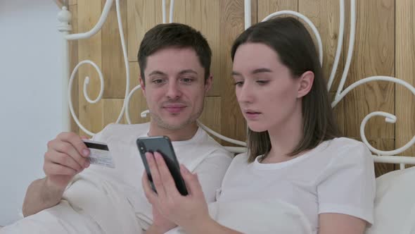 Young Couple Making Online Payment on Smartphone in Bed 