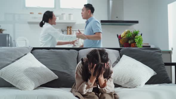 Asian girl kid sitting and crying on bed while parents having fighting or quarrel conflict at home.