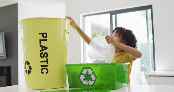 Happy biracial boy sorting plastic bottles and waste in kitchen alt