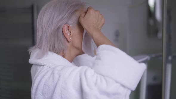 Side View Mature Woman Applying Facial Mask Looking in Mirror in Bathroom