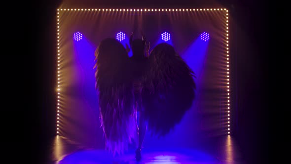 Silhouette of Dancing Greek Goddess Artemis with Wings on Stage in a Dark Studio with Smoke and Neon