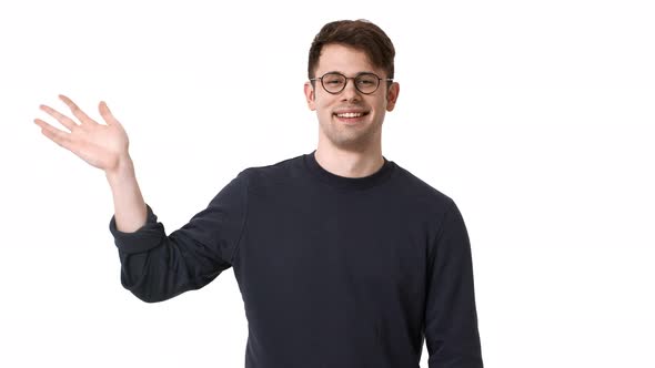 Portrait of Young Man Wearing Black Sweatshirt and Glasses Grinning and Greeting Waving Hand on