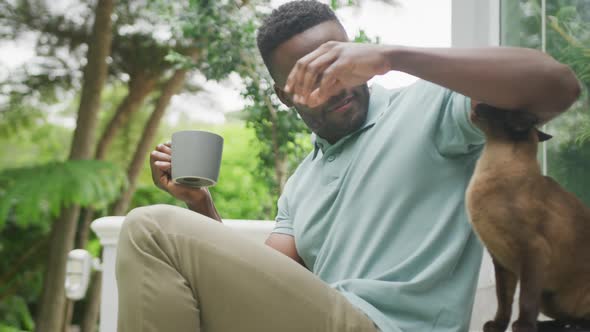 Happy african american man sitting with cat and drinking coffee in garden