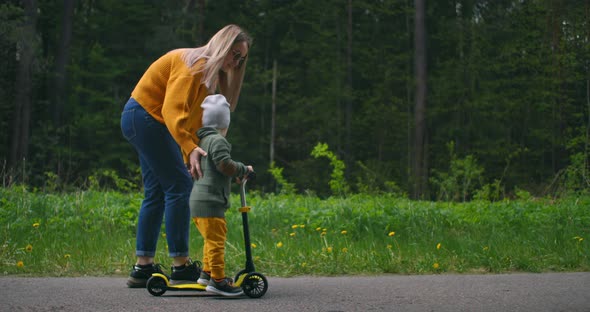 A Young Mother and Her Son Are Learning To Ride a Scooter