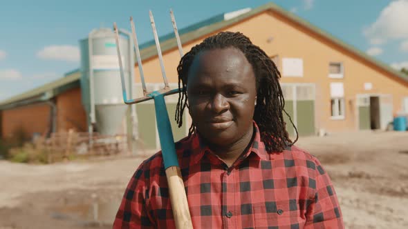 African Farmer Holding Fork Over the Soulder and Nodding His Head in Front of the Silo System 