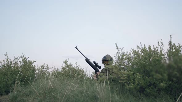 Man in a Military Uniform and a Helmet with a Black Sniper Rifle and Training in the Outdoor Among