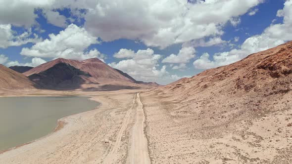 Aerial Over Gravel Off Road Trail Near Arid Desert Mountains in Sunny Day