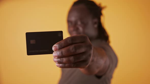 Happy African Man in White Showing Credit Card at Camera Over Orange Background