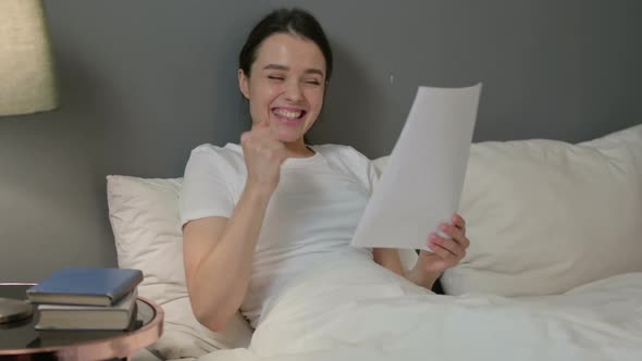 Young Woman Celebrating Success on Documents in Bed