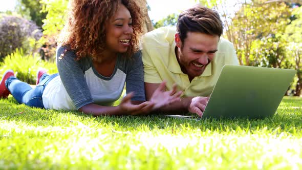 Couple lying on grass and using laptop in park