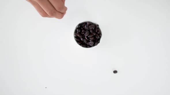 Top down view of throwing coffee bean into white bowl full of beans