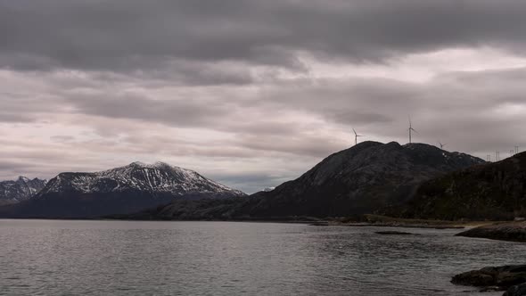 View From Fjord Of Majestic Mountains In Kvaloya Island, Norway. Wind Turbines At Mountain Peak On A