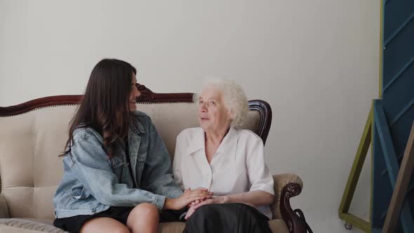 Young Girl Caresses Grandmother's Hands During Pleasant Conversation in Room