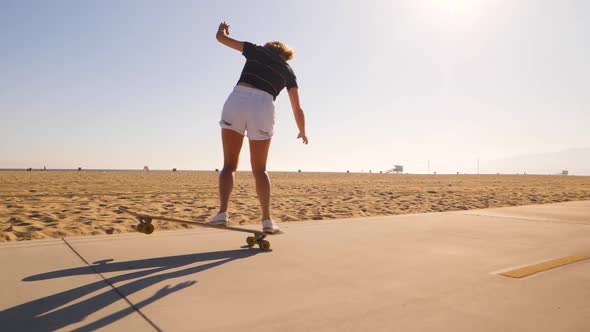 Rear View Of A Sporty Woman Riding Skateboard In Skatepark On Desert Landscape - wide, slow motion