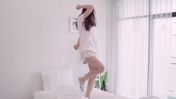 oung Asian woman with headphones dancing while listening music on bed in her bedroom.