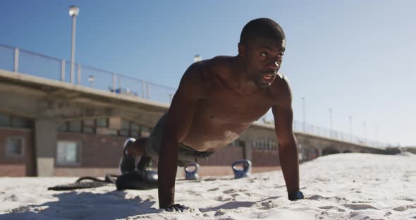 Focused african american man doing press ups, exercising outdoors on beach