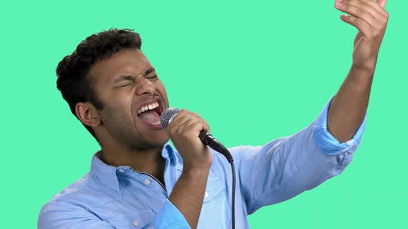 Man Singing Into Microphone on Turquoise Background.