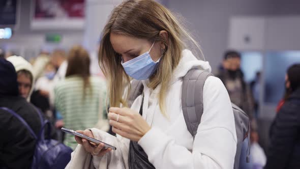 Woman in Mask Using Smartphone While Waiting for Flight in the Airport Crowd