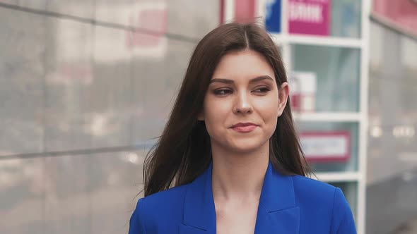 Smiling Woman in Blue Suit Adjusts Hair Walking Along Street