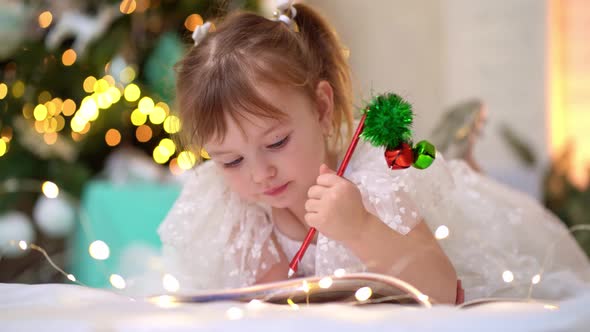 Little Girl Writes a Letter to Santa Claus Under the Christmas Tree