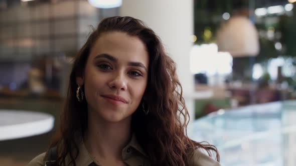 A Girl in a Shopping Mall Adjusts Her Hair and Looks at the Camera