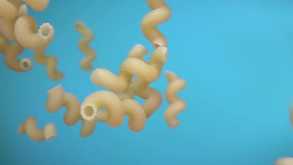 Close-up of Dry Pasta Cellentani Falling Diagonally on the Blue Background