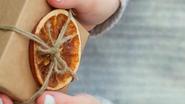 Woman Giving Box with New Year's Gifts Wrapped in Craft Paper and Decorated with Dry Orange Slices