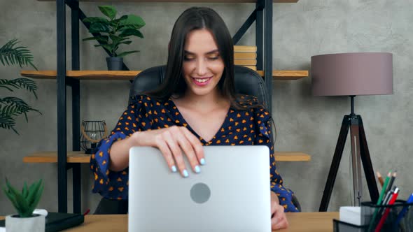 Smiling woman teacher tutor sits on chair at desk in home office opens and starts using laptop