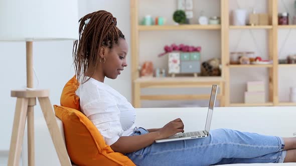 Happy African American Woman is Using Laptop and Typing on Sofa at Modern Interior Spbi
